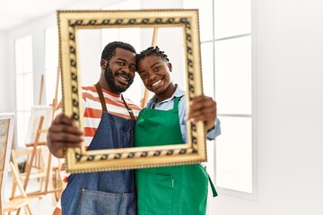 African american painter couple smiling happy holding empty frame at art studio.