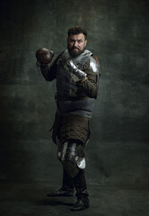Fototapeta na wymiar Portrait of medieval warrior or knight with dirty wounded face boxing gloves isolated over dark background. Comparison of eras, history