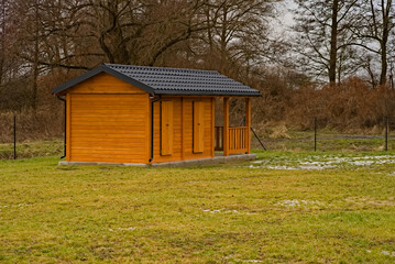 Domek ( altanka )  na trawiastej działce rekreacyjnej na łące i na tle drzew bezlistnych . Cottage (gazebo) on a grassy recreational plot in a meadow and against the background of leafless trees.  © Grzegorz