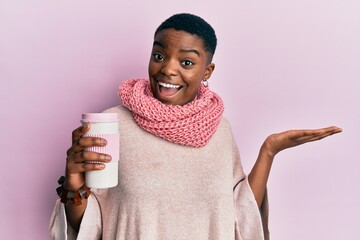 Young african american woman wearing winter scarf and drinking hot take away coffee celebrating...