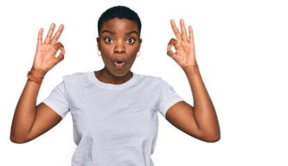 Young african american woman wearing casual white t shirt looking surprised and shocked doing ok approval symbol with fingers. crazy expression