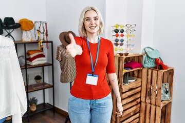 Young caucasian woman working as manager at retail boutique smiling friendly offering handshake as greeting and welcoming. successful business.