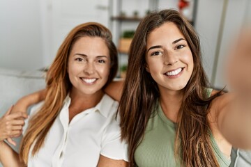 Mother and daughter smiling confident and hugging each other making selfie by the camera at home