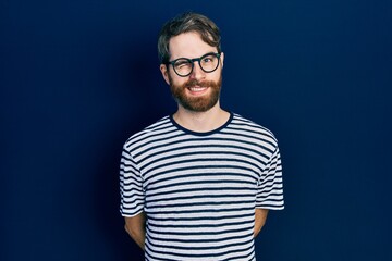 Caucasian man with beard wearing striped t shirt and glasses winking looking at the camera with...