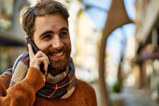 Caucasian man with beard having a conversation speaking on the phone outdoors on a sunny day