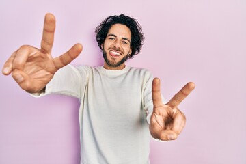 Handsome hispanic man wearing casual white sweater smiling with tongue out showing fingers of both...
