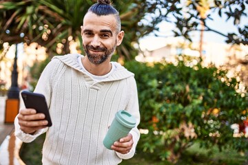 Fototapeta premium Handsome middle age man with beard standing happy and confident outdoors using smartphone
