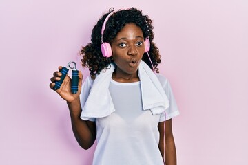 Young african american woman wearing workout clothes and holding hand grip scared and amazed with...