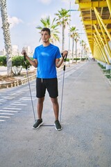 Young hispanic man training with elastic bands outdoors