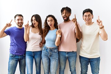 Obraz premium Group of young people standing together over isolated background pointing finger up with successful idea. exited and happy. number one.
