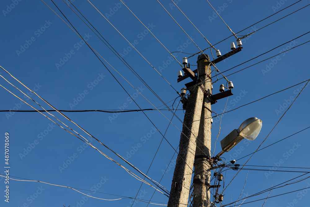 Wall mural electric wires hanging on a pole with a lighting lamp photographed from below on a background of blu