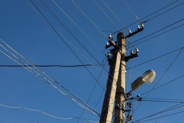 Electric wires hanging on a pole with a lighting lamp photographed from below on a background of...