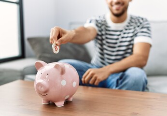 Young arab man smiling confident inserting bitcoin on piggy bank at home