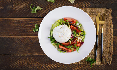 Salad with tomatoes and burrata cheese with lettuce and olive oil on wooden background. Italian cuisine. Top view