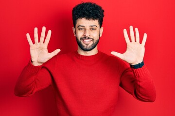 Naklejka premium Young arab man with beard wearing casual red sweater showing and pointing up with fingers number ten while smiling confident and happy.