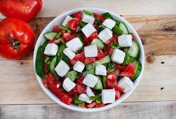 Simple Bulgarian Shopska type salad with tomato, cucumbers, peppers and plain feta. flat lay with light wooden surface and copy space