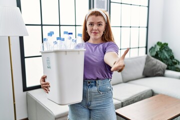 Fototapeta na wymiar Young redhead woman holding recycling wastebasket with plastic bottles smiling friendly offering handshake as greeting and welcoming. successful business.