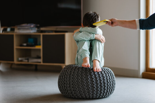 Anonymous parent giving smartphone to offended boy in sleepwear