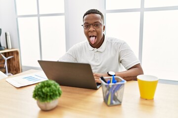 Young african man working at the office using computer laptop sticking tongue out happy with funny expression. emotion concept.