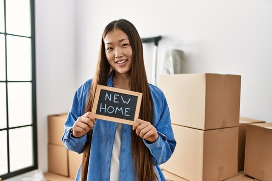 Young chinese girl smiling happy holding blackboard with new home message at new home