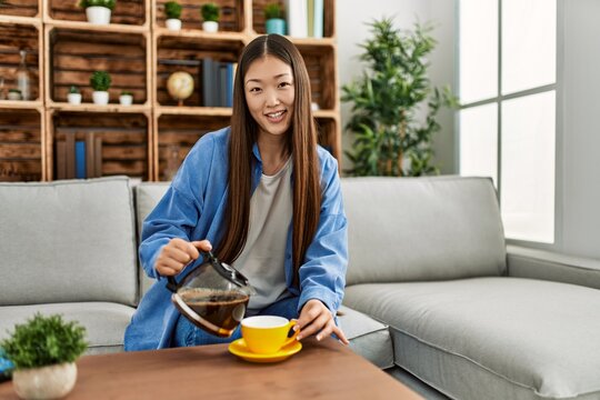 Young chinese girl drinking coffee sitting on the sofa at home.