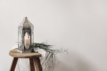 Burning silver Moroccan, Arabic lantern. Dry palm leaf and cotton cloth on wooden stool. Greeting card for Muslim holiday Ramadan Kareem or boho wedding. Festive still life background.