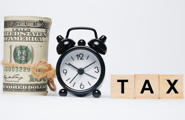 A picture of fake money, alarm clock and wooden block written TAX. Taxation and reminder concept