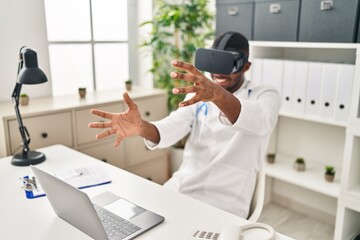 Naklejka na ściany i meble Young african american man wearing doctor uniform using virtual reality glasses at clinic