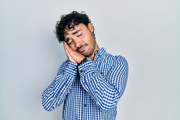 Young hispanic man wearing casual clothes sleeping tired dreaming and posing with hands together while smiling with closed eyes.