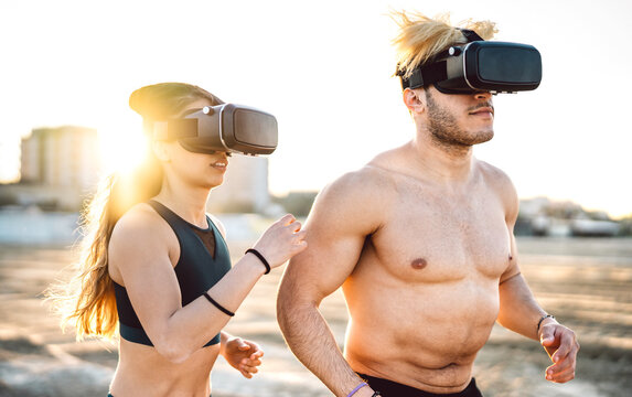 Fitness couple running at beach wearing vr goggle headset - Sport and technology life concept with modern fit people jogging and exercising on trek simulation at summer time - Warm sunhine halo filter