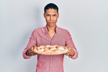 Young african american guy holding tray with cake sweets skeptic and nervous, frowning upset because of problem. negative person.