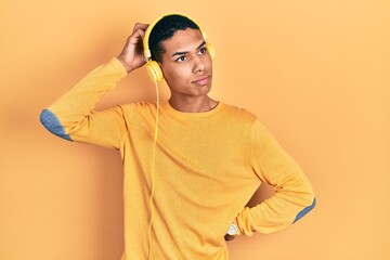 Young african american guy listening to music using headphones confuse and wondering about...