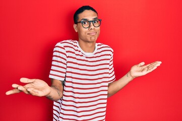 Young african american guy wearing casual clothes and glasses clueless and confused expression with...