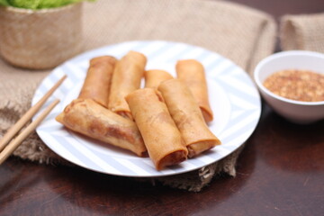 Fried spring rolls with vegetables and tomatoes placed in a black plate on a white wooden table and...