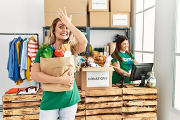 Young blonde woman at volunteer center holding donations paper box stressed and frustrated with hand on head, surprised and angry face