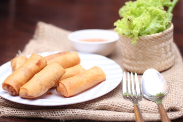 Fried spring rolls with vegetables and tomatoes placed in a black plate on a white wooden table and dipping sauce.