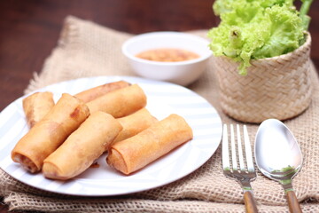 Fried spring rolls with vegetables and tomatoes placed in a black plate on a white wooden table and dipping sauce.