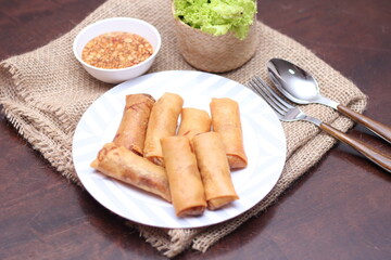 Fried spring rolls with vegetables and tomatoes placed in a black plate on a white wooden table and dipping sauce.