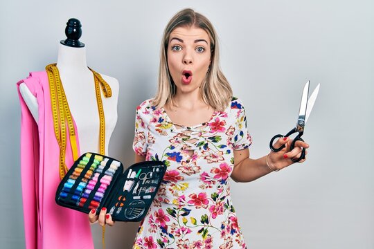 Beautiful caucasian woman dressmaker designer holding scissors and sewing kit afraid and shocked with surprise and amazed expression, fear and excited face.