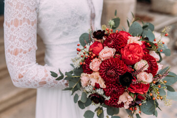 Braut hält wunderschönen herbstlichen Brautstrauß mit roten Blumen und Eukalyptus in ihren Armen