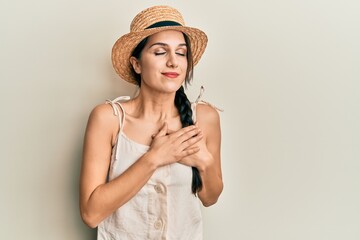 Young hispanic woman wearing summer hat smiling with hands on chest, eyes closed with grateful gesture on face. health concept.