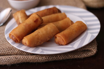 Fried spring rolls with vegetables and tomatoes placed in a black plate on a white wooden table and dipping sauce.