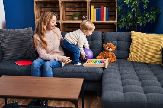 Mother and son playing with ball sitting on sofa at home