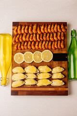 Mussels baked with cheese sauce and sliced lemon and fried shrimps on wooden cutting board with card and glass bottles
