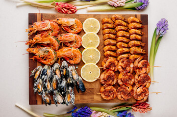 Fried tails of langoustines and fried mussels with sauce and fried shrimps and sliced lemon on wooden cutting board and jacinths