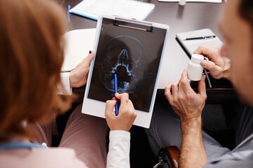 Young female radiologist pointing at mri scan image of human head during consultation with her...