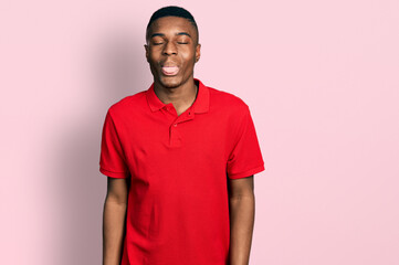 Young african american man wearing casual red t shirt sticking tongue out happy with funny expression. emotion concept.