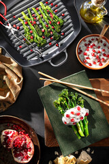 Char-grilled long-stem broccoli, Broccolini, Bimi seared in griddle pan served with herbal yoghurt and pomegranate seeds. Flatlay.