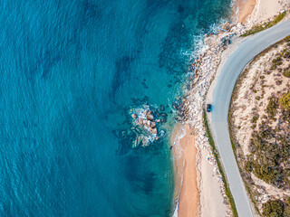 Aerial view of an idyllic sea sandy beach with asphalt winding road and small car driving on. Background for travel and vacation - Powered by Adobe