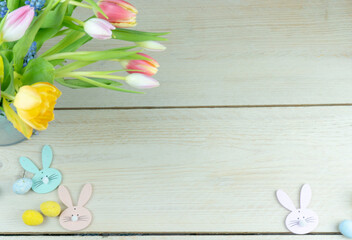 Wielkanocna karta z kwiatami i króliczkami na tle jasnych desek.